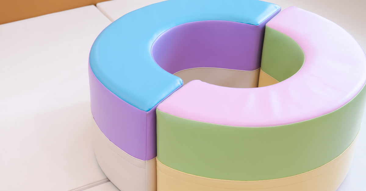 A soft play area for children with plastic mats, walls, and two crescent-shaped cushions that create a circle.
