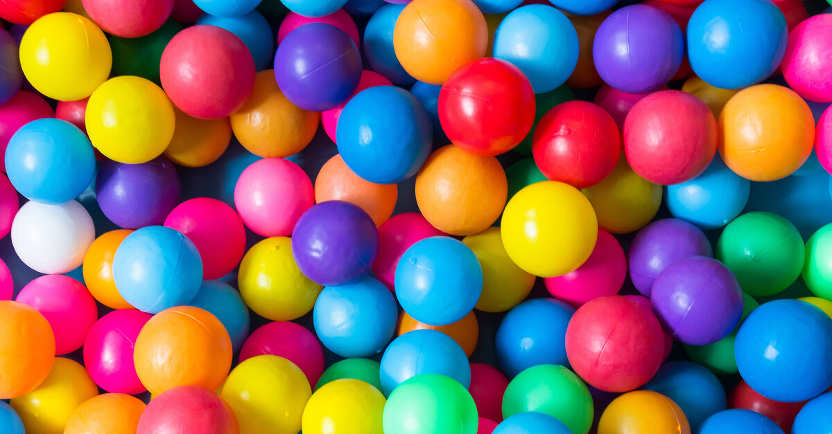 Multiple plastic balls piled on top of each other in a large ball pit. The balls are all the colors of the rainbow.