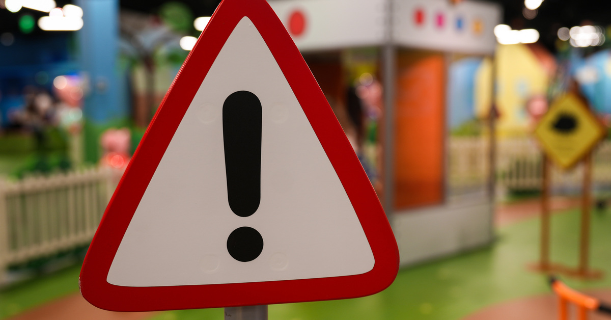 A triangular sign with a red border, white body, and an exclamation point in the center is at an indoor playground.