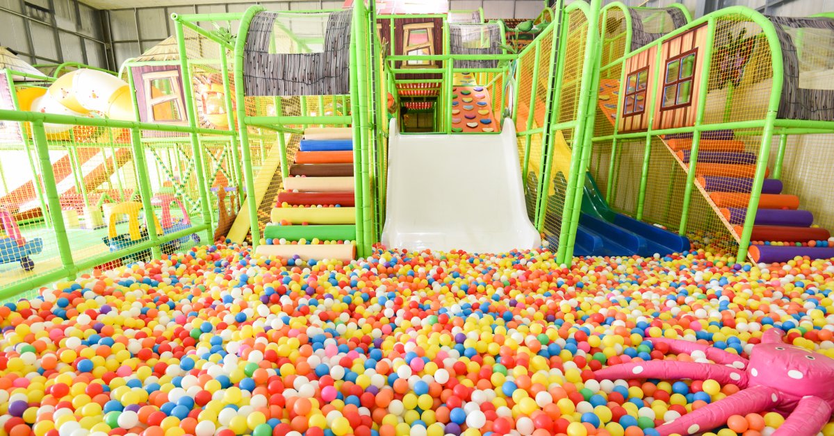 A large ball bit filled with colorful balls within an indoor playground, with four low-profile slides in the middle.